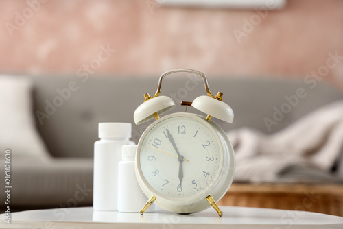 Obraz na plátne Alarm clock with pill bottles on table in room, closeup