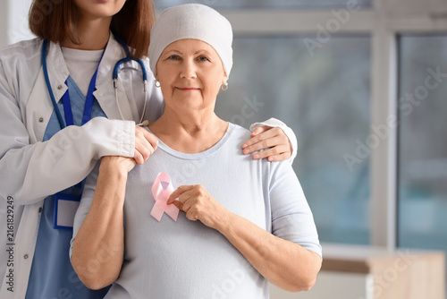 Senior woman after chemotherapy with pink ribbon and doctor hugging in clinic...