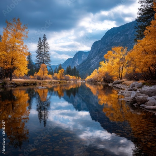 A serene river flowing through a valley during autumn, with vibrant yellow and orange trees reflecting in the calm water against a backdrop of towering granite mountains under a dramatic cloudy sky.