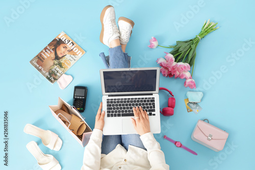 Woman with laptop and tulips shopping online on blue background, top view