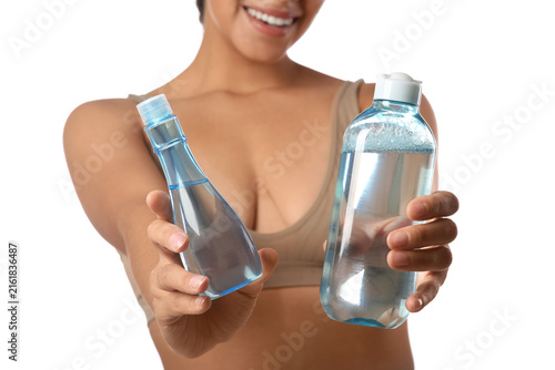 Young African-American woman with bottles of micellar water on white background