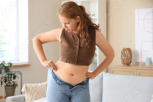 Young woman in tight jeans at home. Weight gain concept