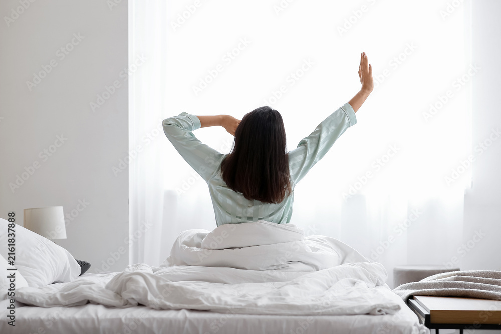 Fototapeta premium Morning of young beautiful sleepy woman in bedroom at home, back view