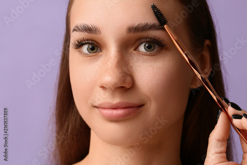 Plakat w ramie Young woman correcting shape of her eyebrows on lilac background, closeup