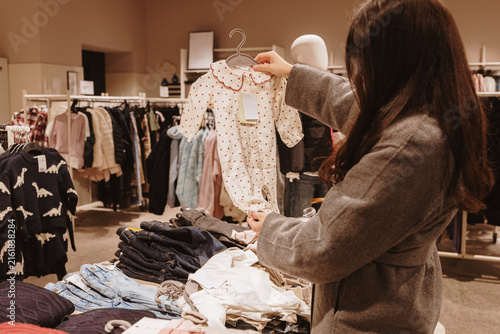A girl holds beautiful bodysuits for a newborn baby while standing in a store.