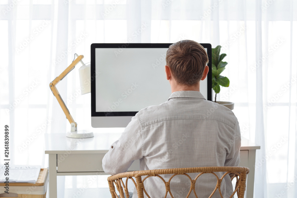 Fototapeta premium Young man using computer at table in office, back view