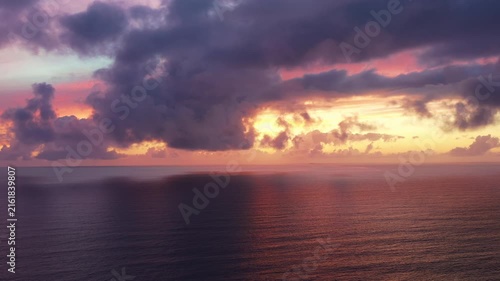 Vibrant sunset over the Atlantic Ocean with dramatic illuminated clouds reflecting on calm water, creating a colorful evening seascape.