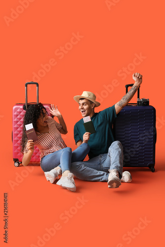 Cheerful couple of tourists with suitcases and passports on orange background
