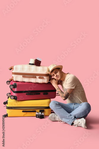 Young male tourist with many suitcases sitting on pink background