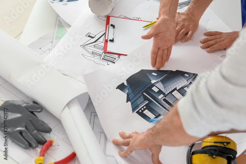 Team of male builders working with house plan in room, closeup