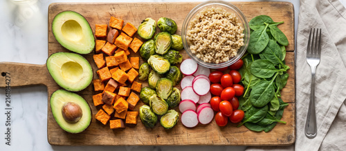 Fresh vegetables and grains arranged on a wooden cutting board in a kitchen setting
