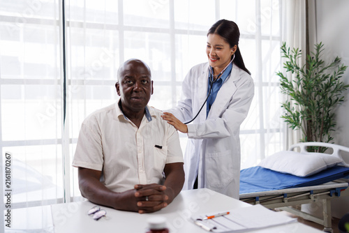 Canvastavla Female doctor in white coat performing a medical checkup on a smiling senior afr