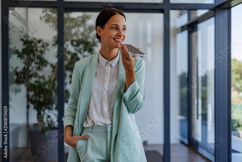 Businesswoman talking on phone with voice assistant in modern office, communicating and networking with smart technology