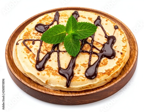 Stack of golden pancakes, drizzled with chocolate and garnished with mint on a wooden plate