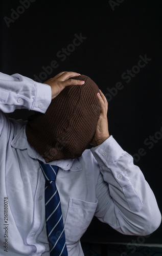 Quadro su tela A disguised Asian male wearing a brown knitted ski mask clutches the head with both hands in a dramatic expression of extreme stress, panic, or overwhelming despair