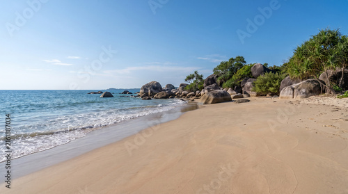 Tropical beach with turquoise water and rocky coastline under clear sky.