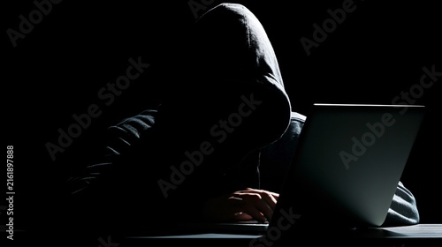 Professional Hooded Hacker Working on Laptop in Dramatic Low Key Lighting