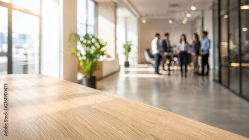 Modern Office Lobby: A sunlit, spacious office lobby with a focus on a polished wooden reception desk, blurred background figures of professionals standing near large windows.