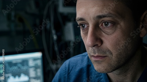 Tired male doctor looking at medical monitor in hospital at night