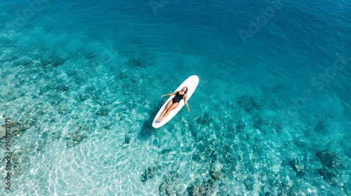 Woman lying on a paddleboard in crystal clear blue tropical ocean water