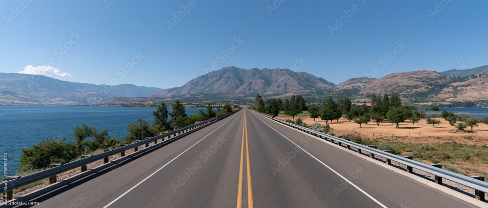 Obraz premium Straight forward‑reaching highway natural scenery, lake distant mountains blue sky white clouds, open countryside road for road trip travel 