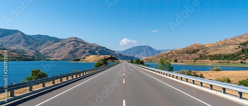 Straight forward‑reaching highway natural scenery, lake distant mountains blue sky white clouds, open countryside road for road trip travel