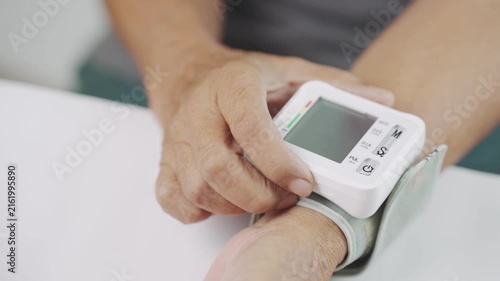 Close up of a senior pressing the start button on a digital wrist blood pressure monitor, representing home blood pressure monitoring, hypertension management, preventive healthcare, selfcare.