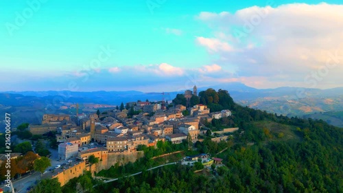 Interesting aerial push-in tilt-down shot in Santa Vittoria in Matenano, the tightly-knit town centre surrounded by rich vegetation, perched on a sumptuous, lofty hill, between ravines, hills, clouds
