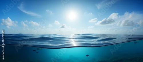 Obraz  z motywem A split-level view showing the bright sun and blue sky above the water surface and the deep blue, clear ocean water below the horizon
