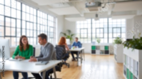 Two colleagues sitting at a white desk in a bright airy modern office environment having a professional discussion while working on laptops and reviewing business documents together