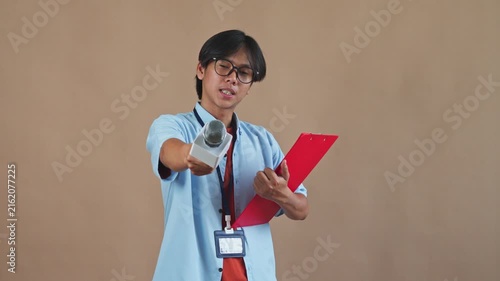 Young Asian male reporter holding red clipboard extends microphone toward camera to conduct interview