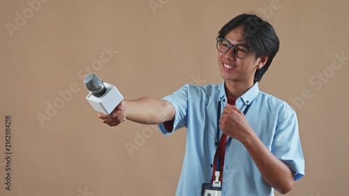 Asian male reporter extends microphone sideways to conduct an interview off-camera in studio background