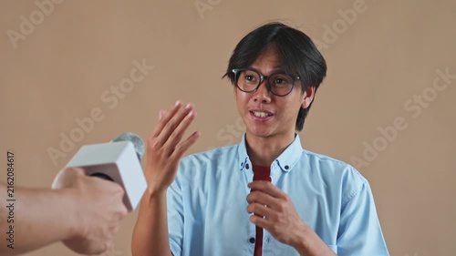 Young Asian man with glasses smiling and talking during studio interview