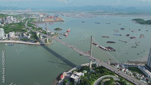 Drone view of Ha Long, Quang Ninh, showing a coastal bridge, harbor, vessels, waterways, urban development, and scenic bay landscape in Vietnam.