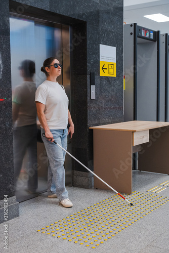 A blind woman exits an elevator. 