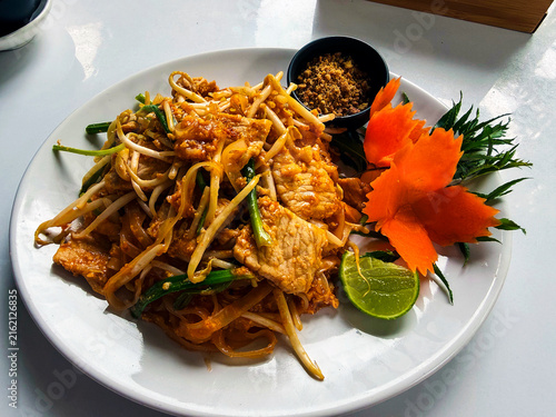 Traditional Thai Pad Thai noodles with pork, bean sprouts, lime, and crushed peanuts on a white plate