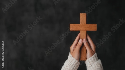 A person holds a wooden cross in both hands against a dark background, symbolizing faith, prayer, and spirituality.
