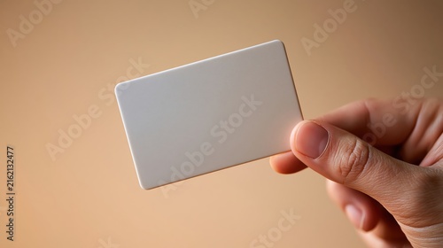Blank white plastic identification card held in human hand against soft beige background for business branding and design mockups