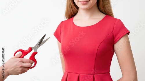 A person holding sharp scissors near a woman wearing vibrant red dress isolated against a plain white studio background