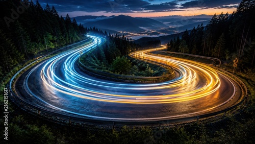 A winding mountain road at twilight with long exposure light trails in blue and yellow colors curving through a dense forest landscape at night