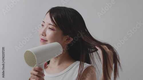 ドライヤーの風で長い髪を乾かす笑顔の女性