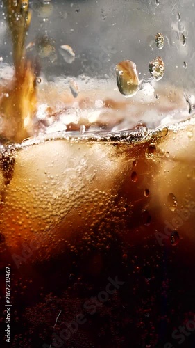 Slow motion vertical pouring cola with ice cubes and bubbles, soft drink