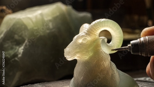Jade Ram Sculpture Creation: A skilled artisan meticulously carves a delicate jade sculpture of a ram, its spiraling horns taking shape under the precise touch of a rotary tool.