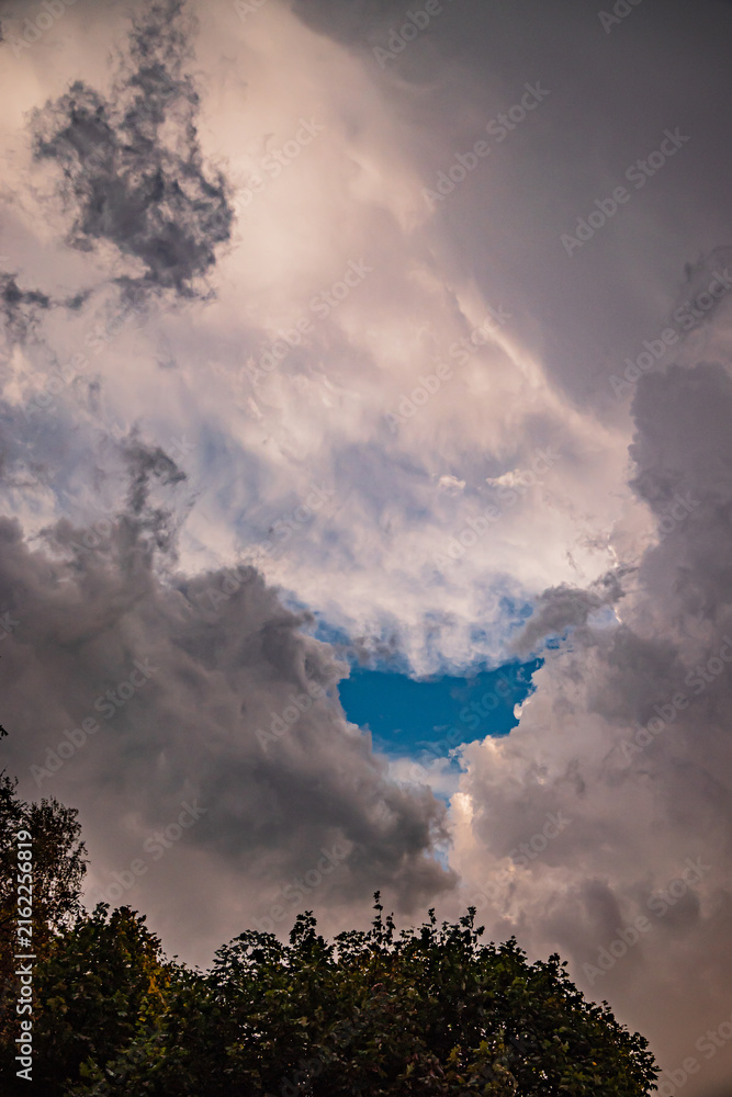 Fototapeta premium Dark clouds part to reveal a vibrant patch of blue sky above a serene landscape