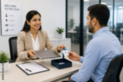 Blurred New Employee Receiving A Laptop And Access Badge During Corporate Onboarding