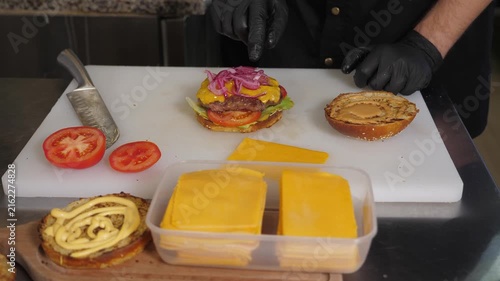 Close-up of the chef putting a red onion on a bun with sauce and a cutlet in the kitchen of a restaurant, the process of making a burger, fast food.