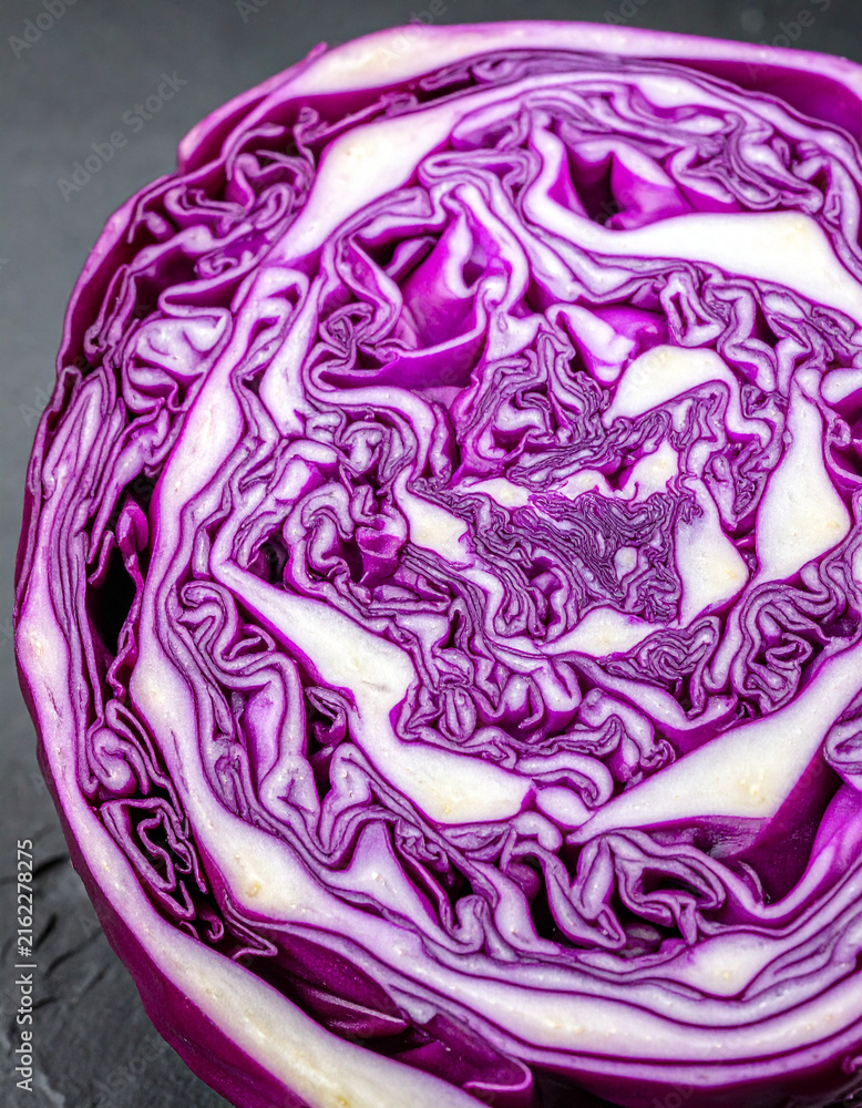 Obraz premium Macro cross section of a purple cabbage showing brain like geometric patterns on a dark stone surface.
