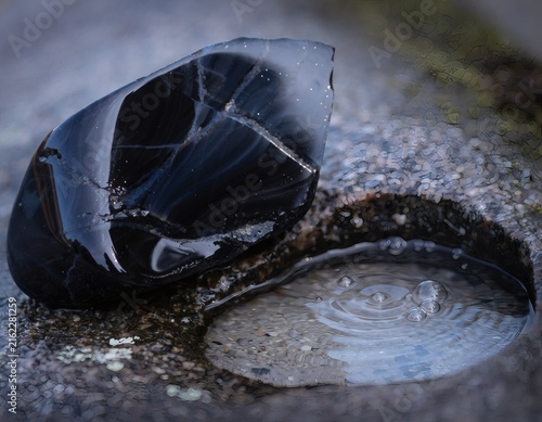 Obsidian Stone Beside Puddle with Rippling Raindrops Capturing a Fleeting Moment