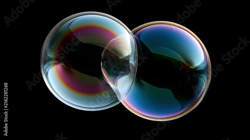 Two soap bubbles joined together displaying iridescent rainbow colors against a black background