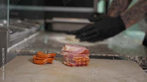 The chef, wearing gloves, is rolling out round dough on a metal table. Pizza making process in the restaurant kitchen. The ingredients for pizzas are lying on the foreground.